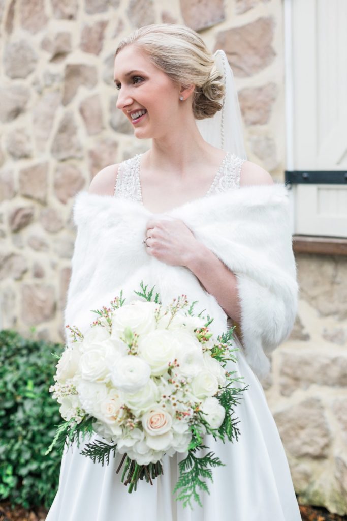 Bride wearing white fur wrap holding white floral bouquet at wedding venue the Inn at Leola Village by the Jepsons