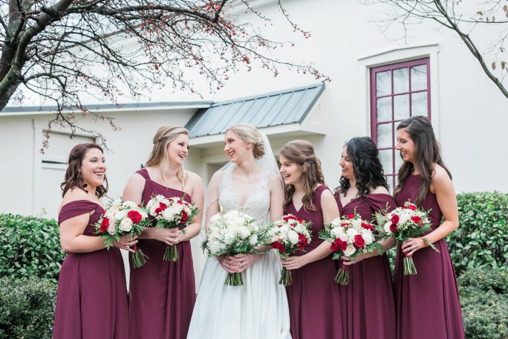 Bride laughing with bridesmaids holding white and red florals at the Inn at Leola Village by the Jepsons