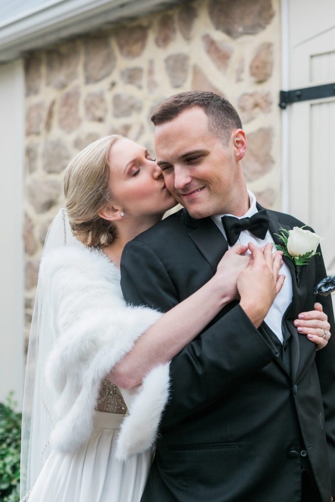 Bride in white fur wrap hugging groom with black bow tie at the Inn at Leola Village by the Jepsons