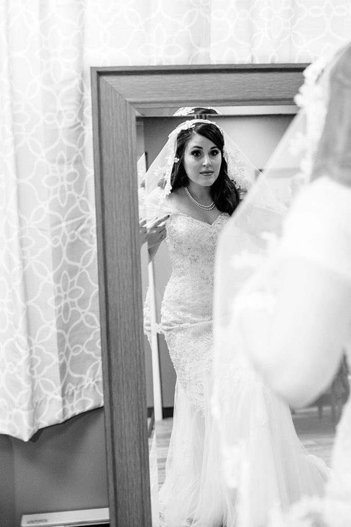 bride putting on lace veil in mirror by the Jepsons