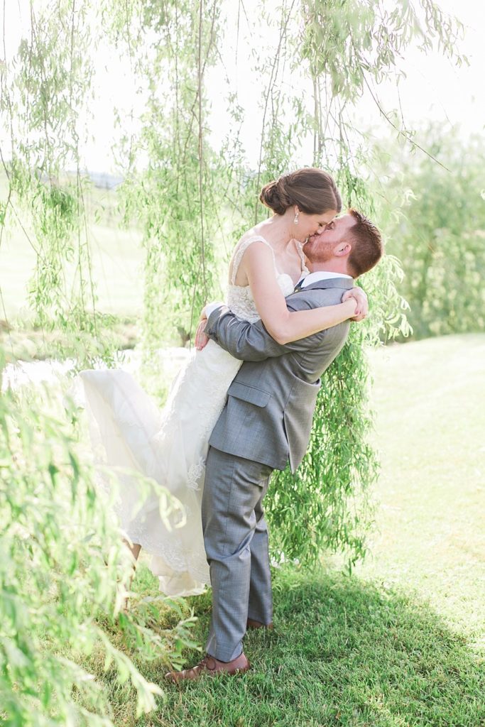 Groom lifts and kisses bride under willow tree at Gillbrook Farms by the Jepsons