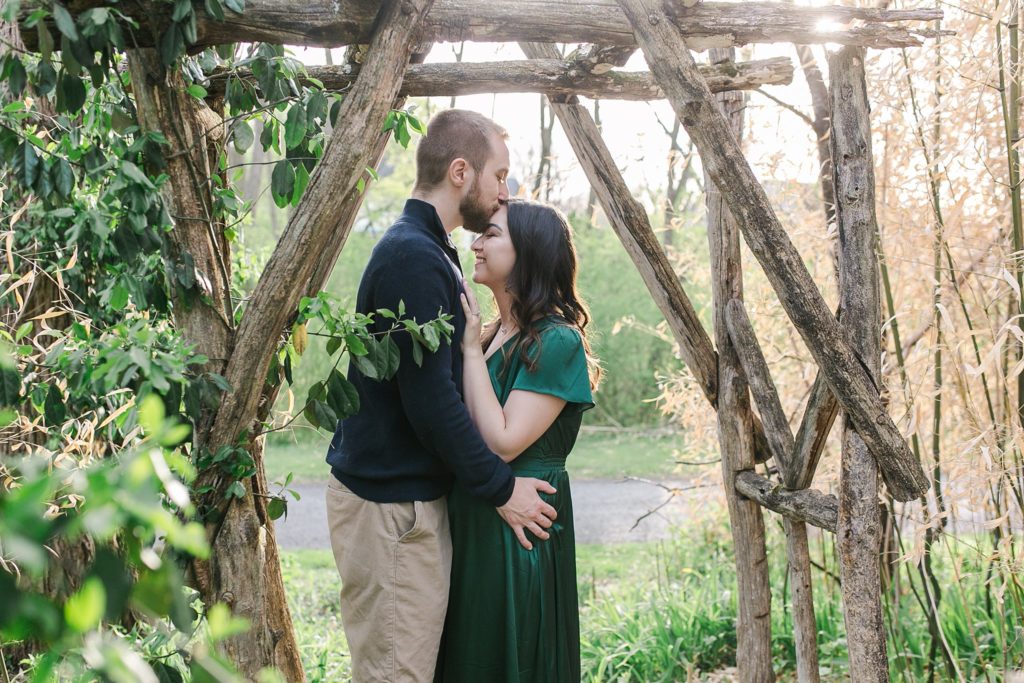 Groom kissing fiancé's forehead while embracing under trellis in State College, PA