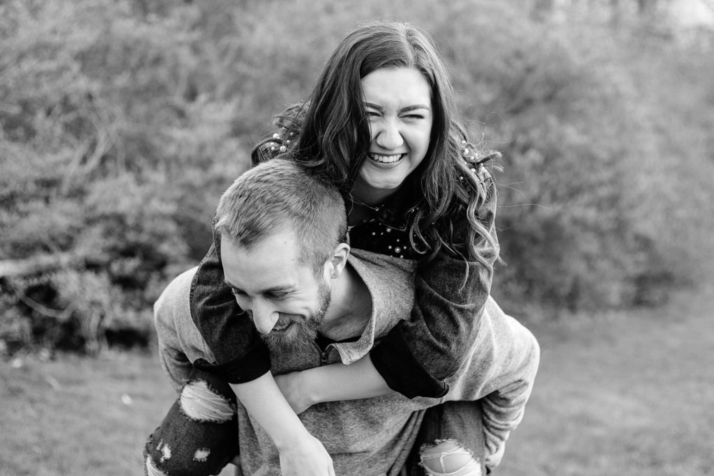 Groom laughs as he holds fiancée piggyback in State College, PA park.